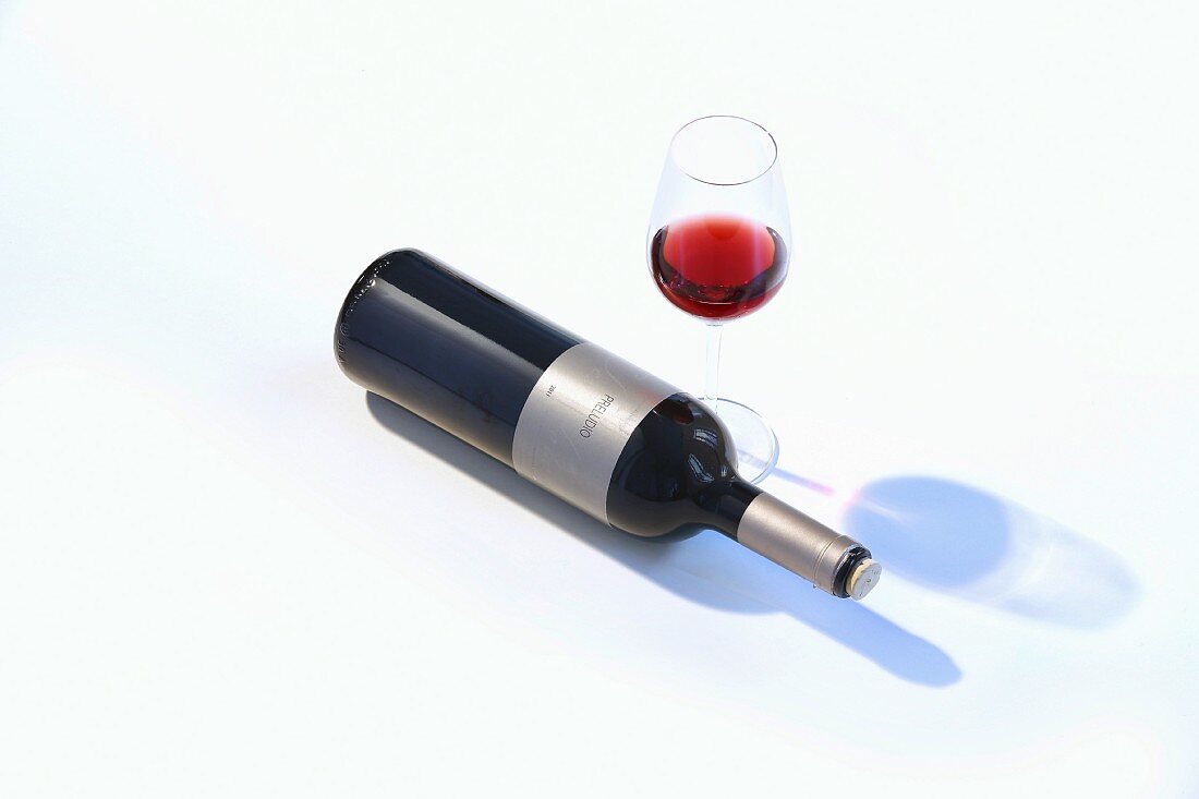 A glass of red wine and a bottle of wine lying on its side