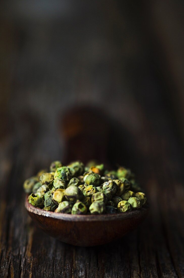 Green peppercorns on a wooden spoon (close-up)