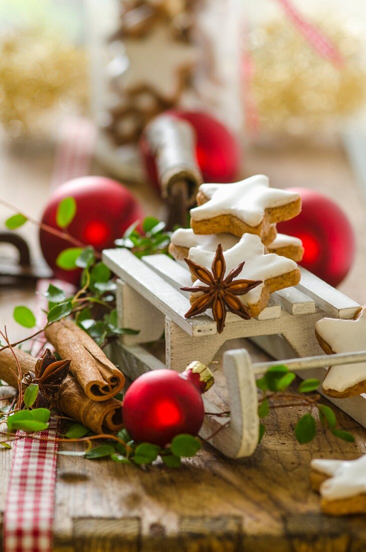Weihnachtsdekoration mit Miniatur-Schlitten, Zimtsternen und Kugeln