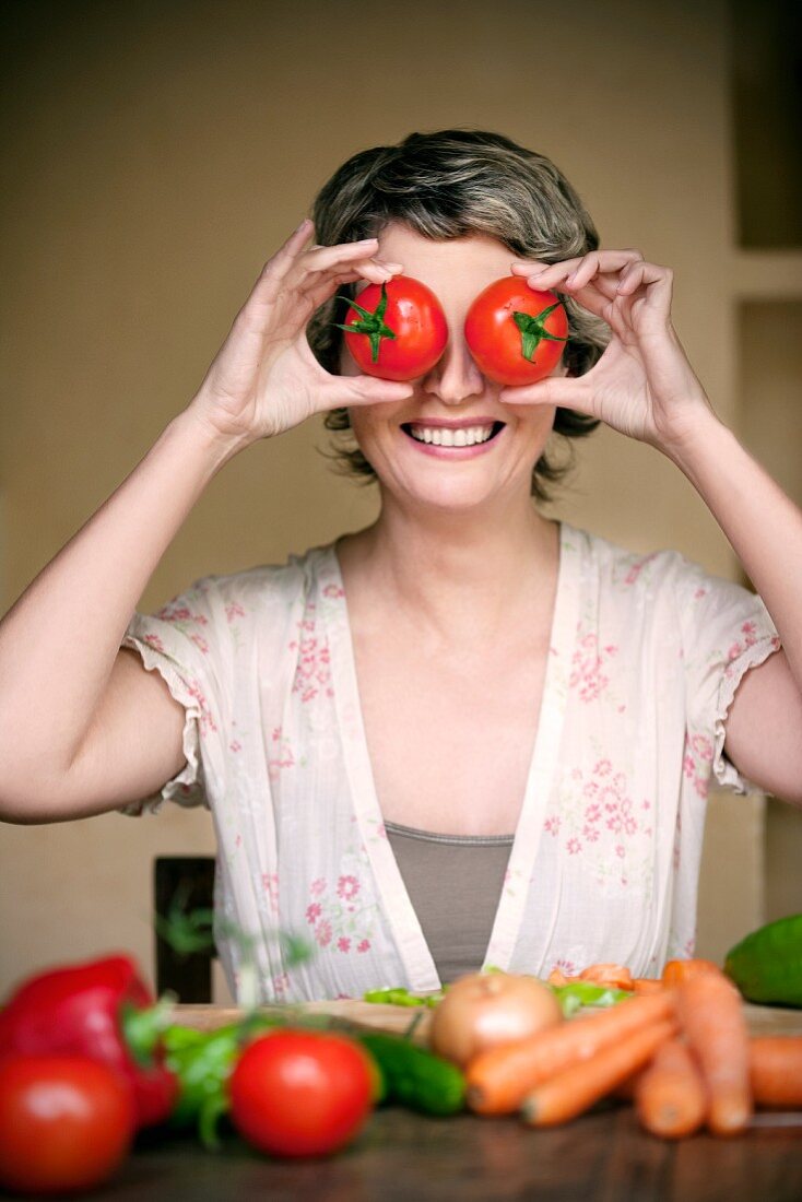 Portrait einer lächelnden Frau die sich zwei Tomaten vor die Augen hält