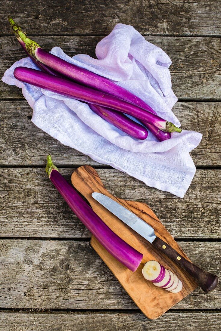 Aubergines on a cloth and on a wooden board, partially sliced