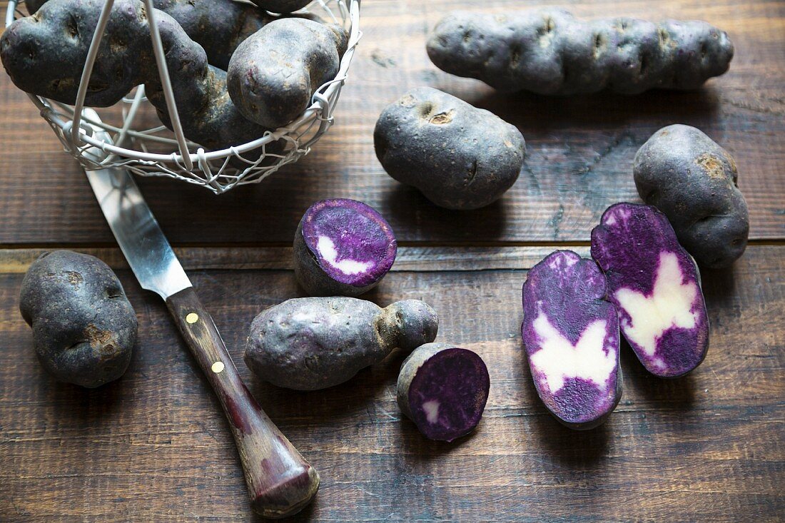 Purple potatoes, whole and halved, on a wooden surface