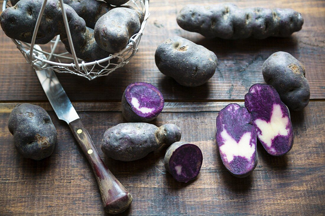 Violette Kartoffeln, ganz und halbiert auf Holzuntergrund