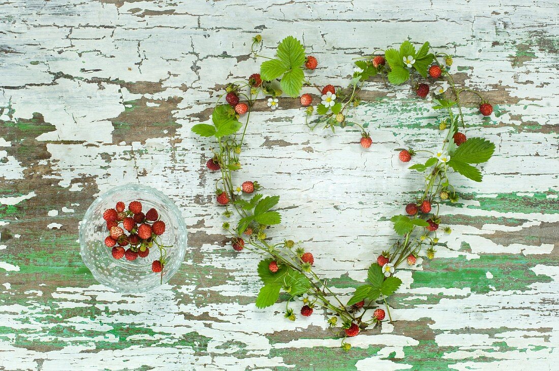 A heart made from wild strawberries, strawberry leaves and flowers on a wooden surface