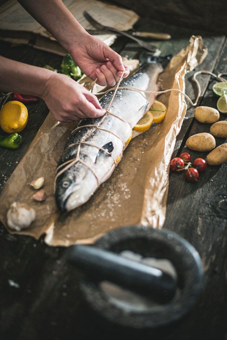 Raw stuffed salmon being tied with kitchen twine