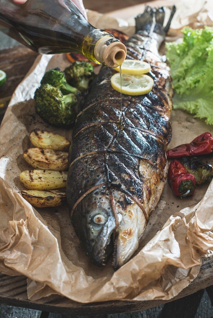 A whole roasted salmon being drizzled with olive oil