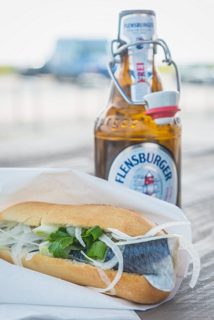 A fish roll and a bottle of beer outside on the table (Sylt, Germany)