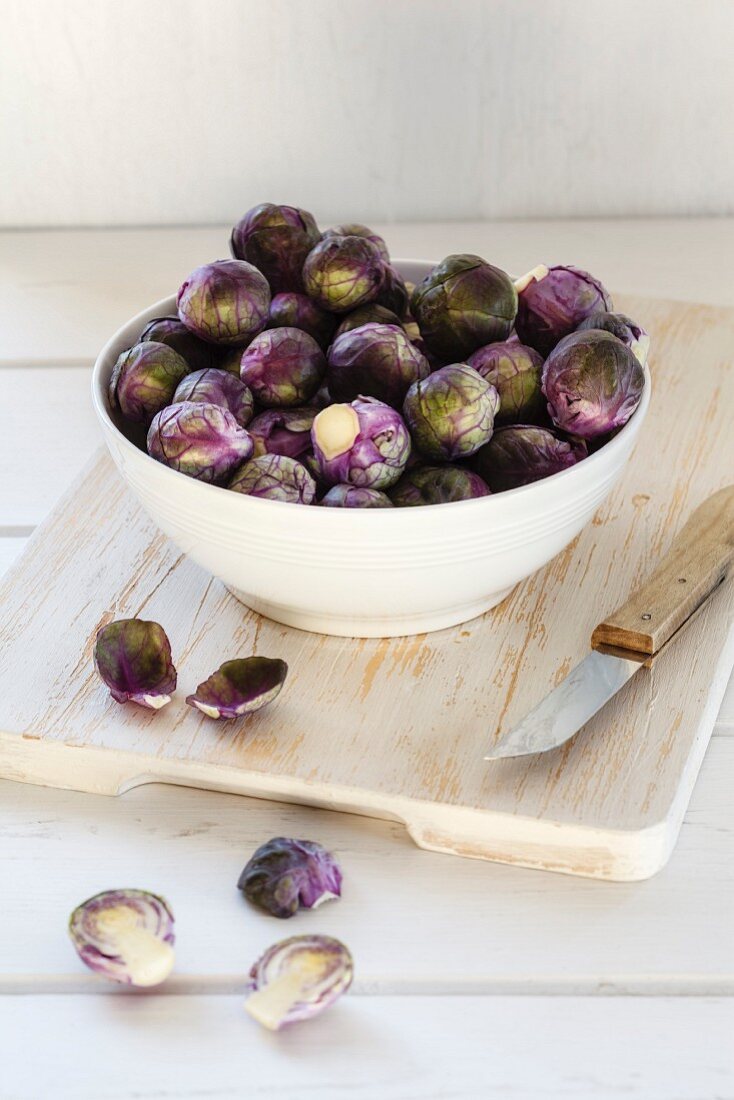 Fresh red Brussels sprouts in a bowl on a wooden chopping board