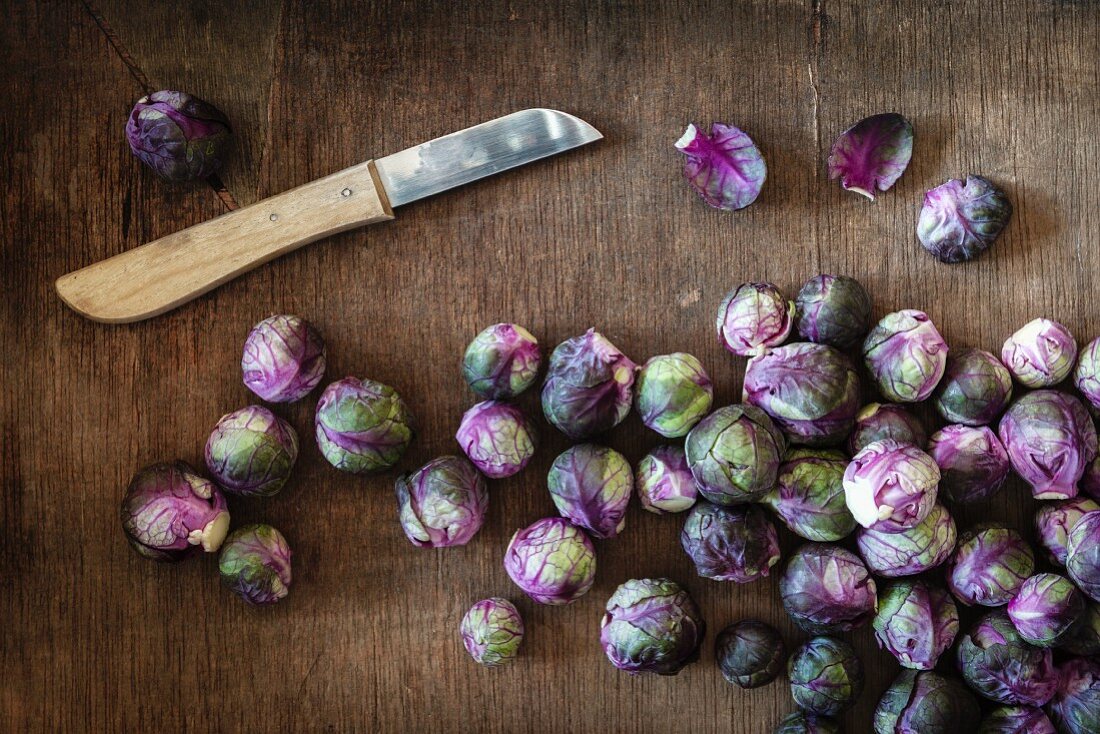 Fresh red Brussels sprouts with a knife on a wooden surface (seen from above)