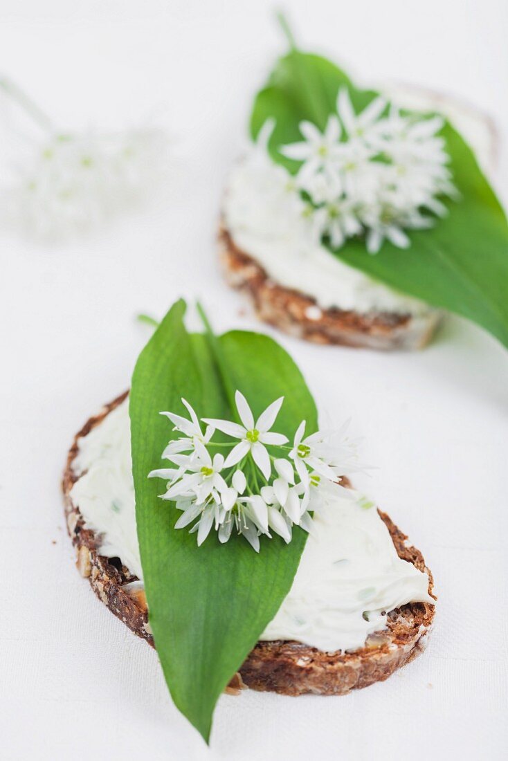 Slices of bread topped with cream cheese, wild garlic leaves and edible wild garlic flowers