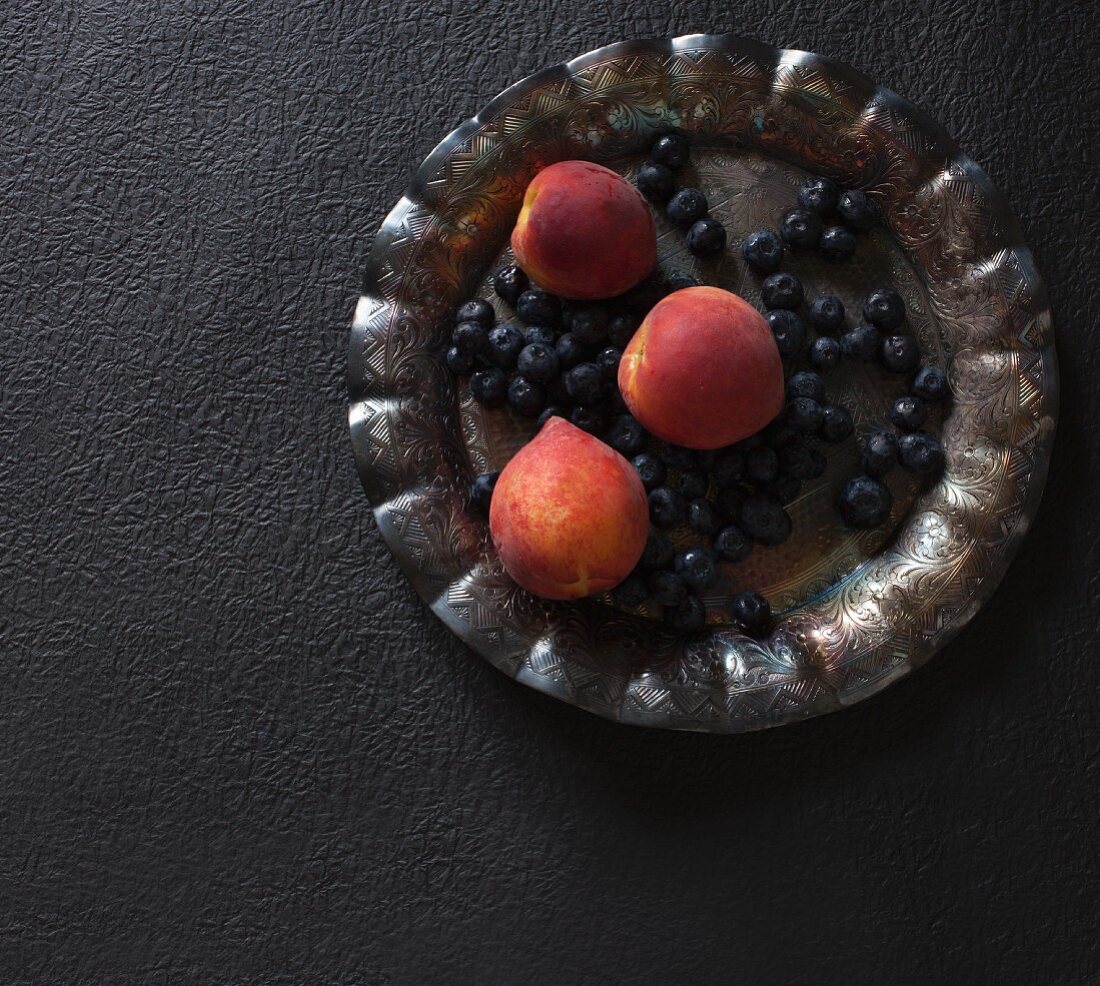 Fresh blueberries and peaches on a metal plate (seen above)