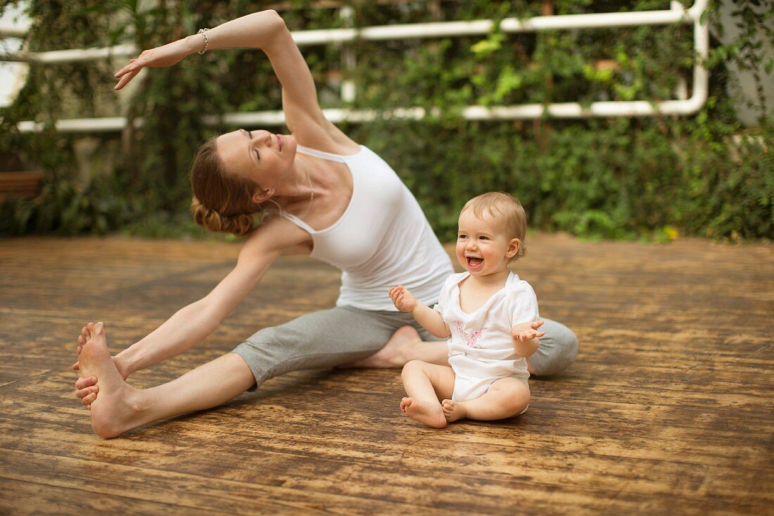 A woman practising yoga while her baby laughs