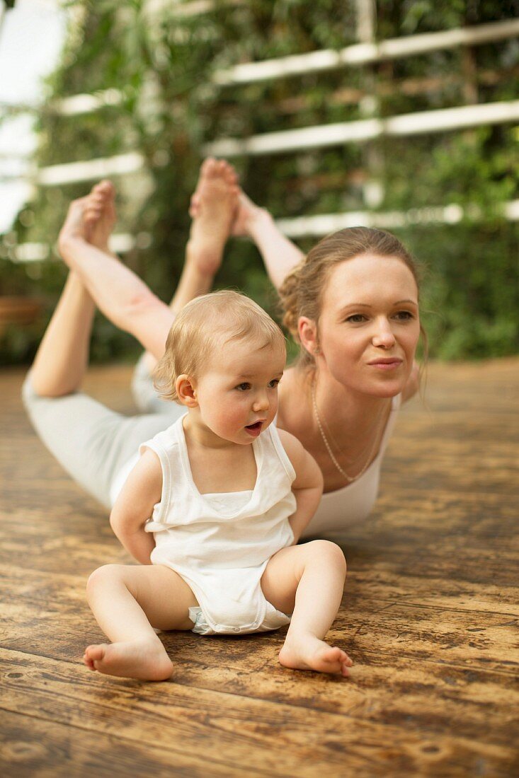Frau macht Yoga-Übung während Baby daneben sitzt