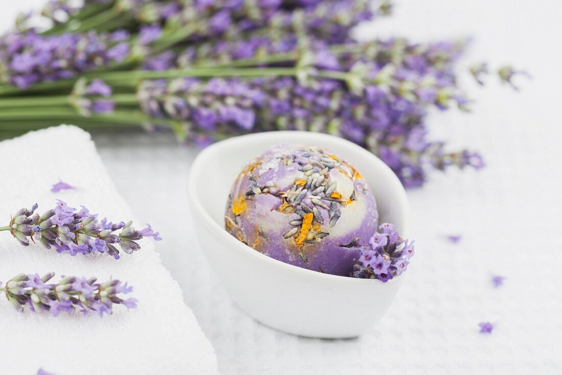 A ball of lavender-calendula soap in a bowl with lavender and a white towel