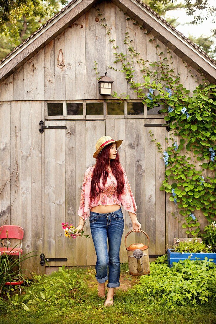 A young girl wearing a hippie outfit with a watering can and flowers in a garden