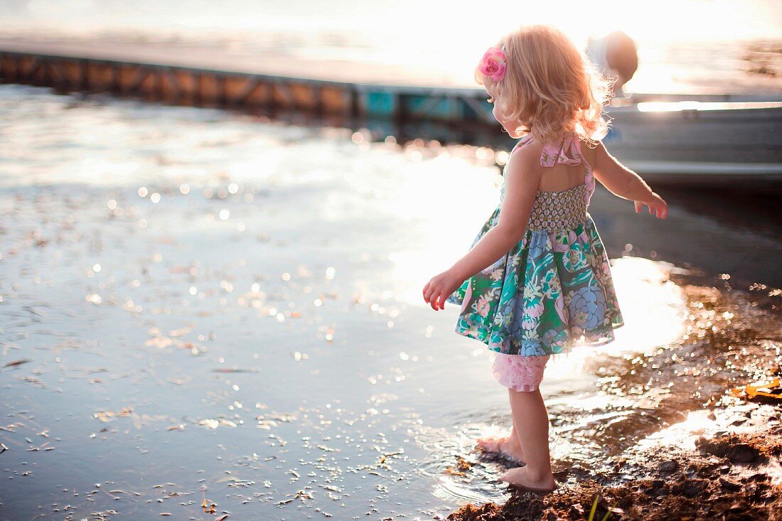 A little girl wearing a dress dipping a toe in a rural lake