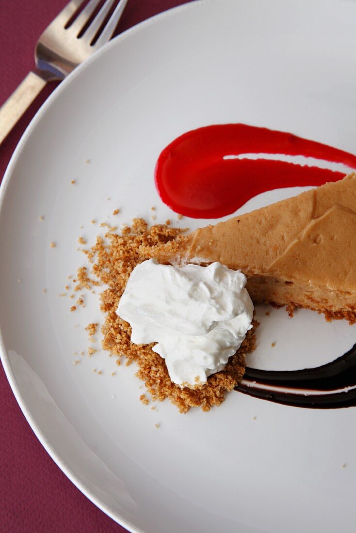 A slice of peanut butter pie with fruit sauce and cream (seen from above)