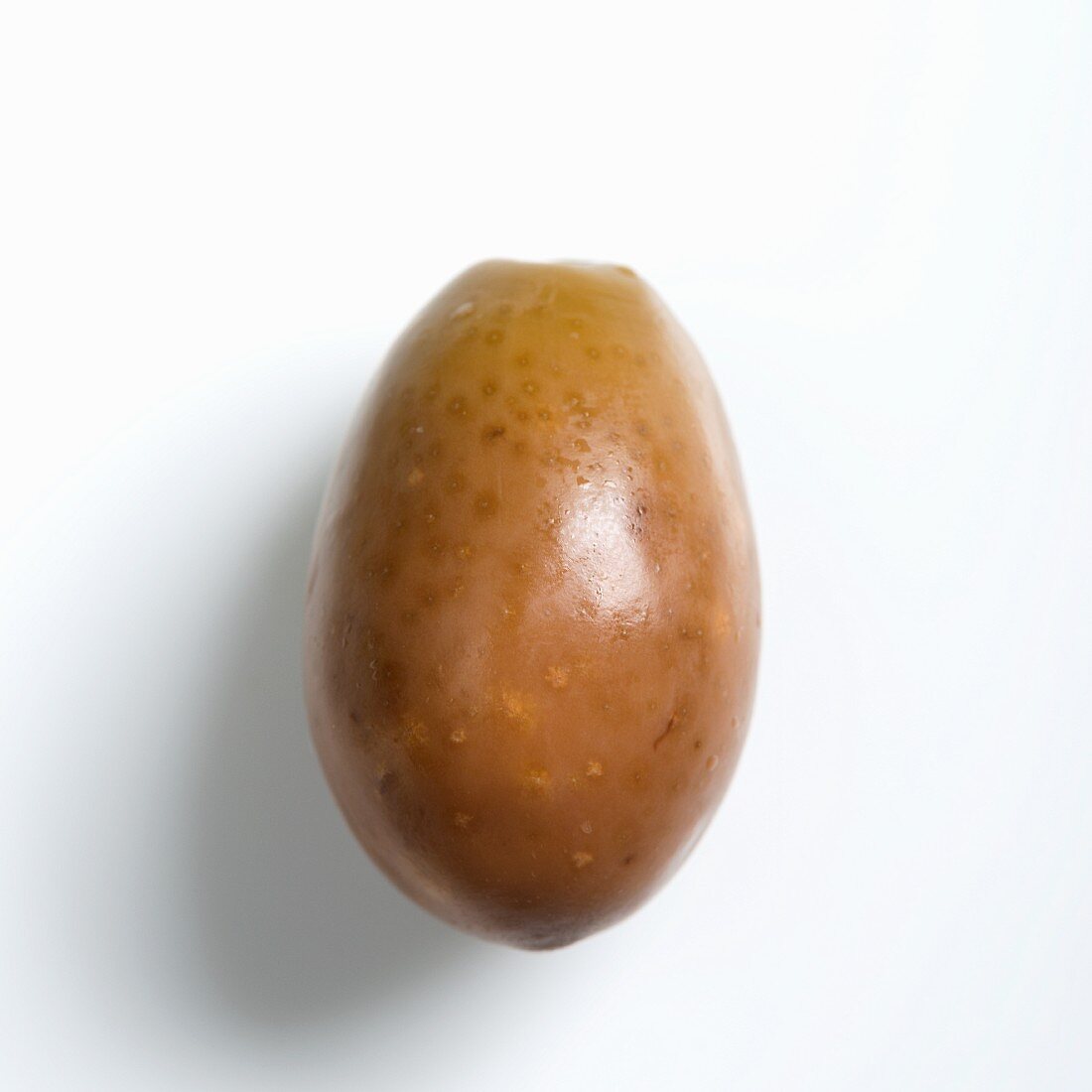 A green olive on a white surface