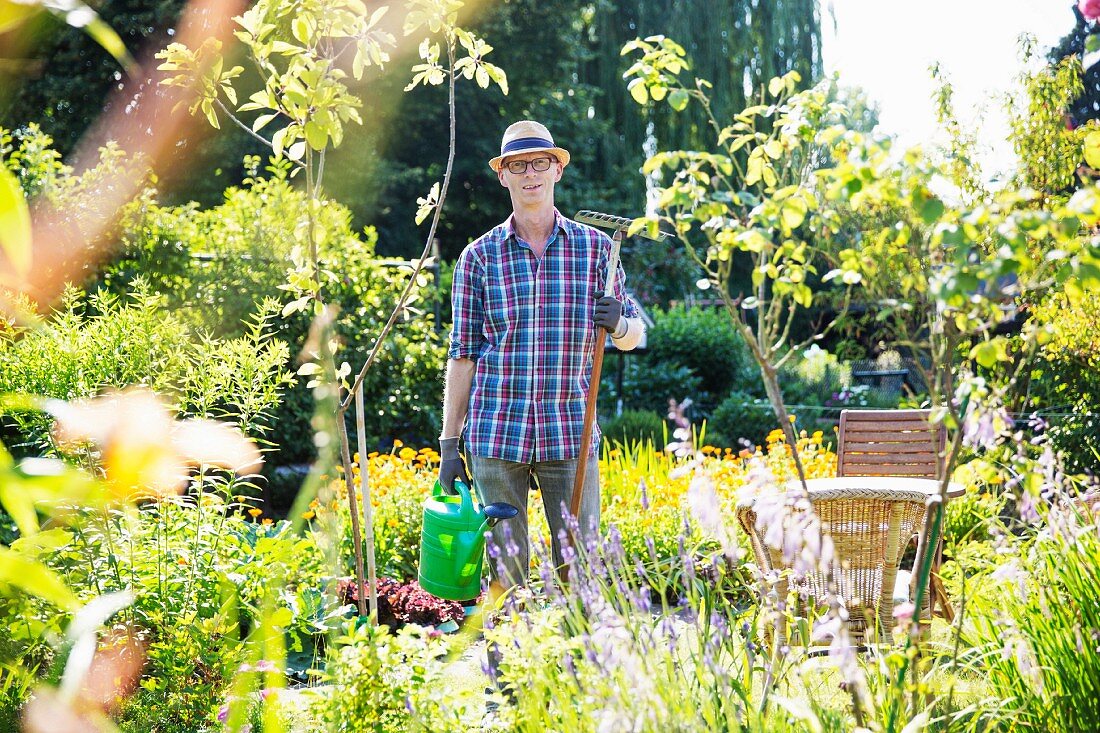 Mann mit Rechen und Gießkanne im Sommergarten