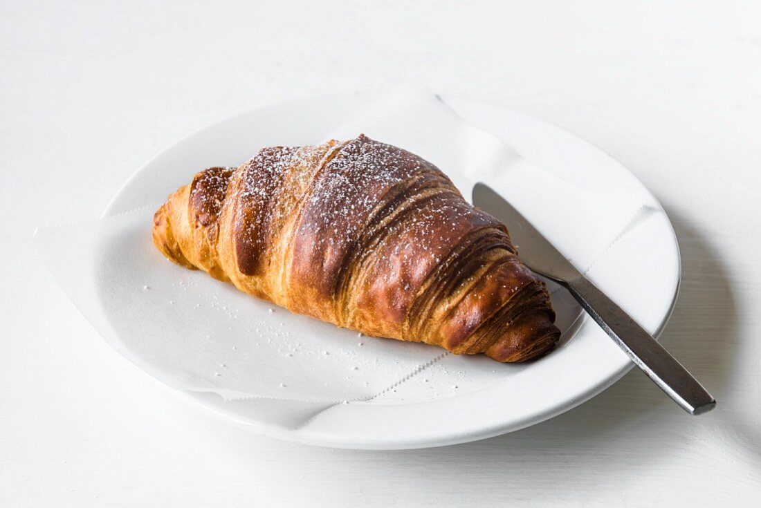 A croissant on a white plate with a knife