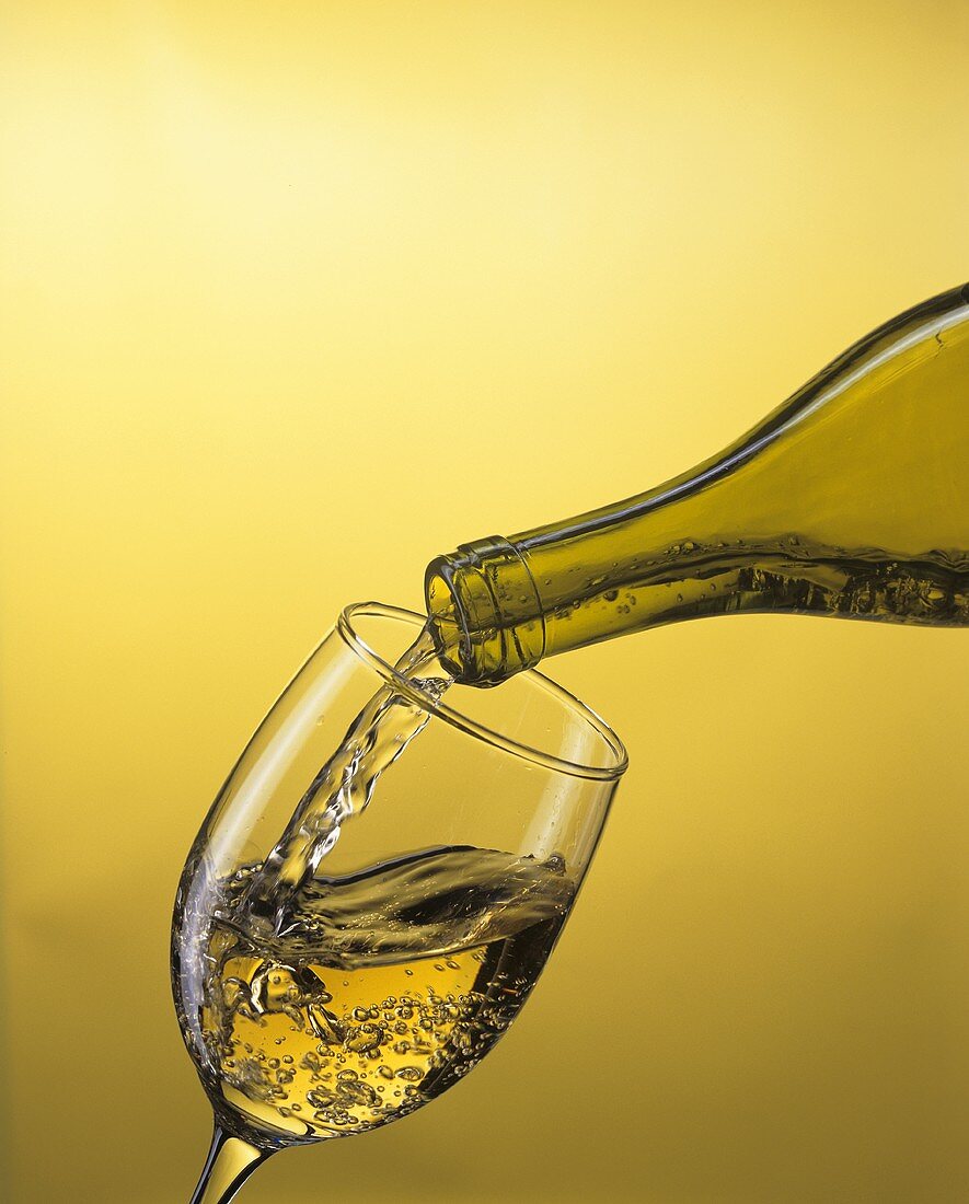 Weißwein aus der Flasche in ein Glas gießen