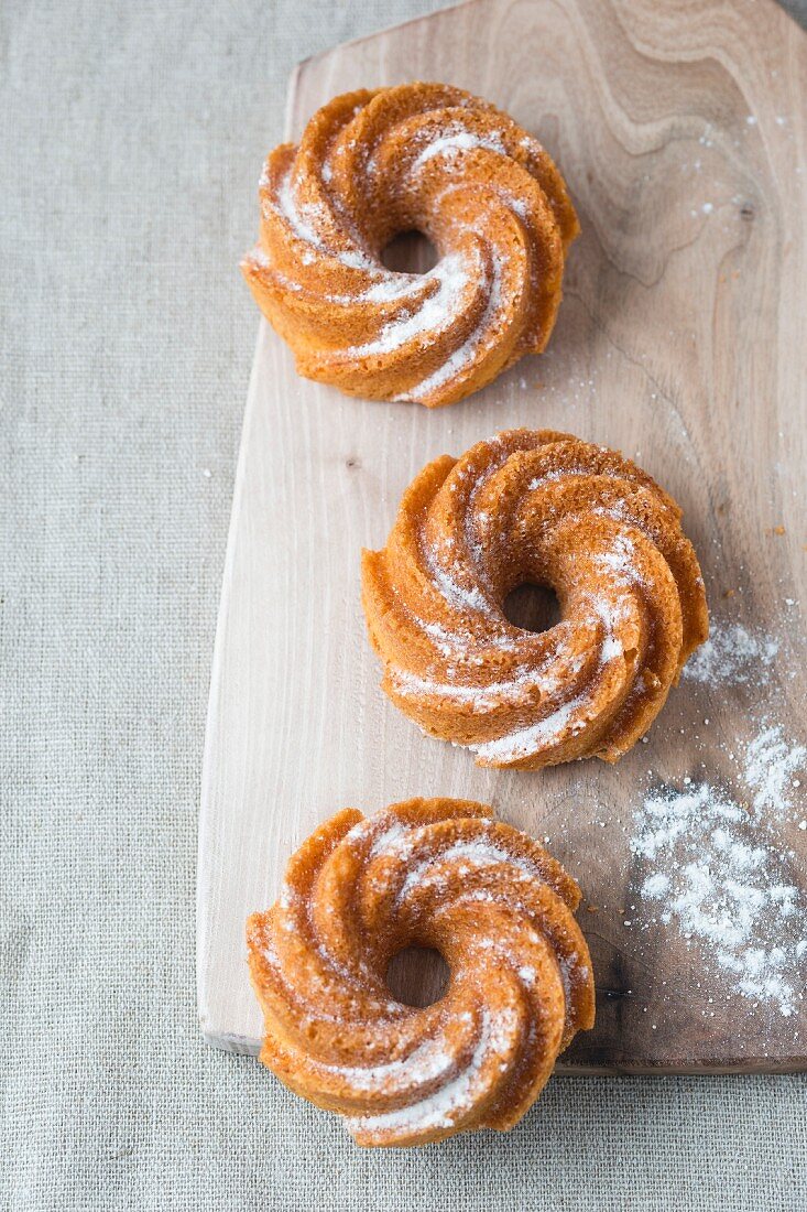 Drei Mini-Kranzkuchen mit Puderzucker auf Holzbrett