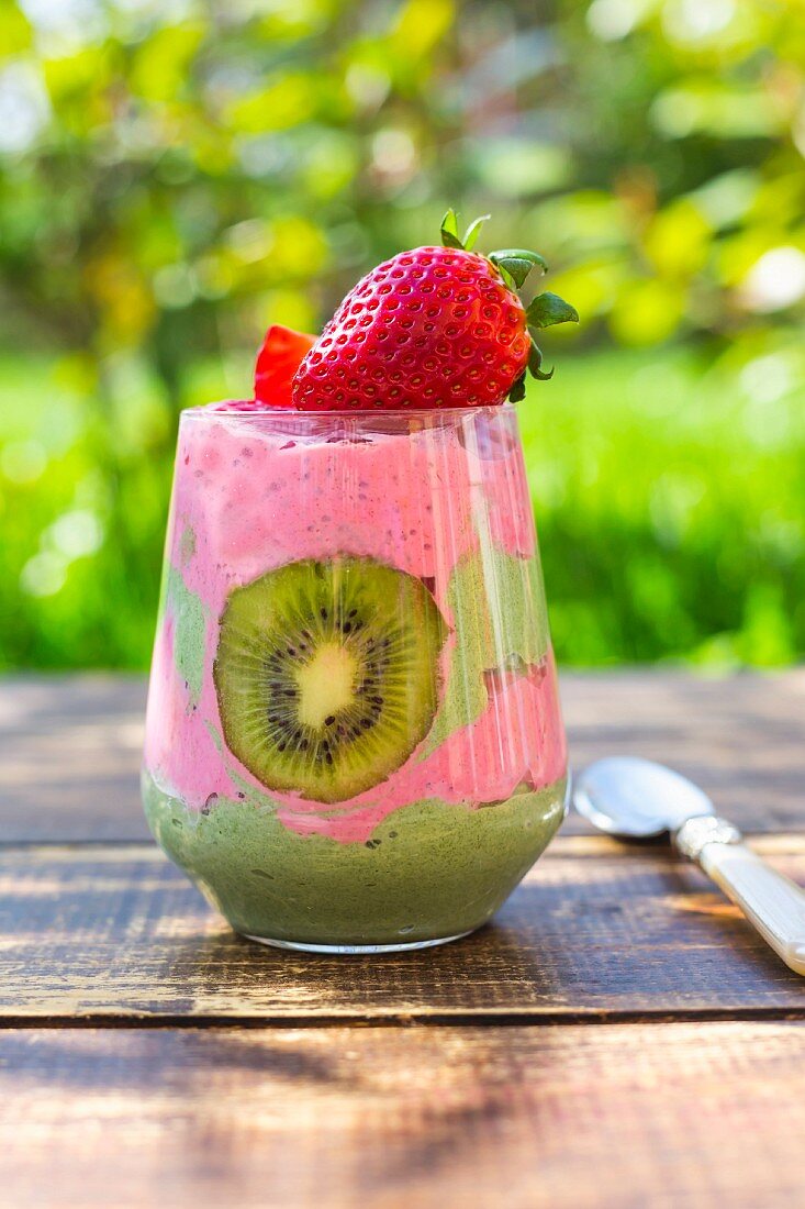 A glass of chia pudding with kiwi and strawberries on a table outside