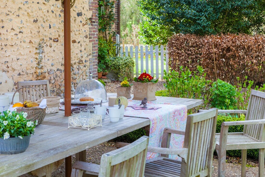Gedeckter Gartentisch mit Frühlingsblumen und Holzstühlen auf Terrasse mit ländlichem Flair