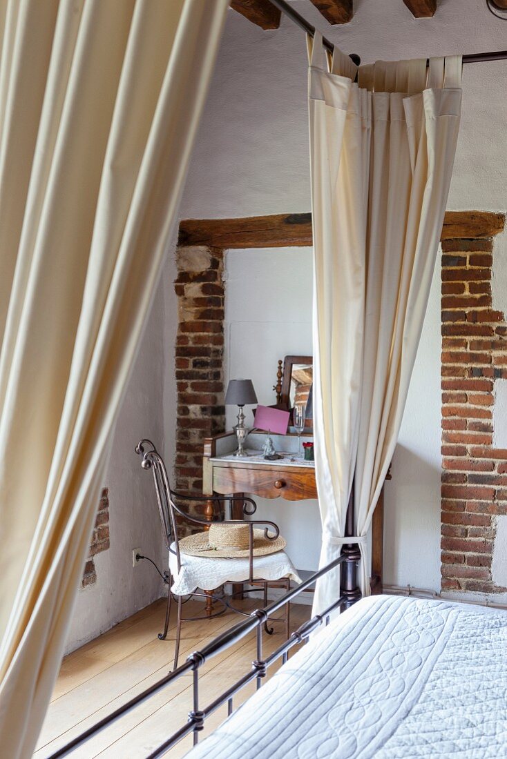 Canopied bed in front of vintage-style dressing table and armchair in renovated farmhouse