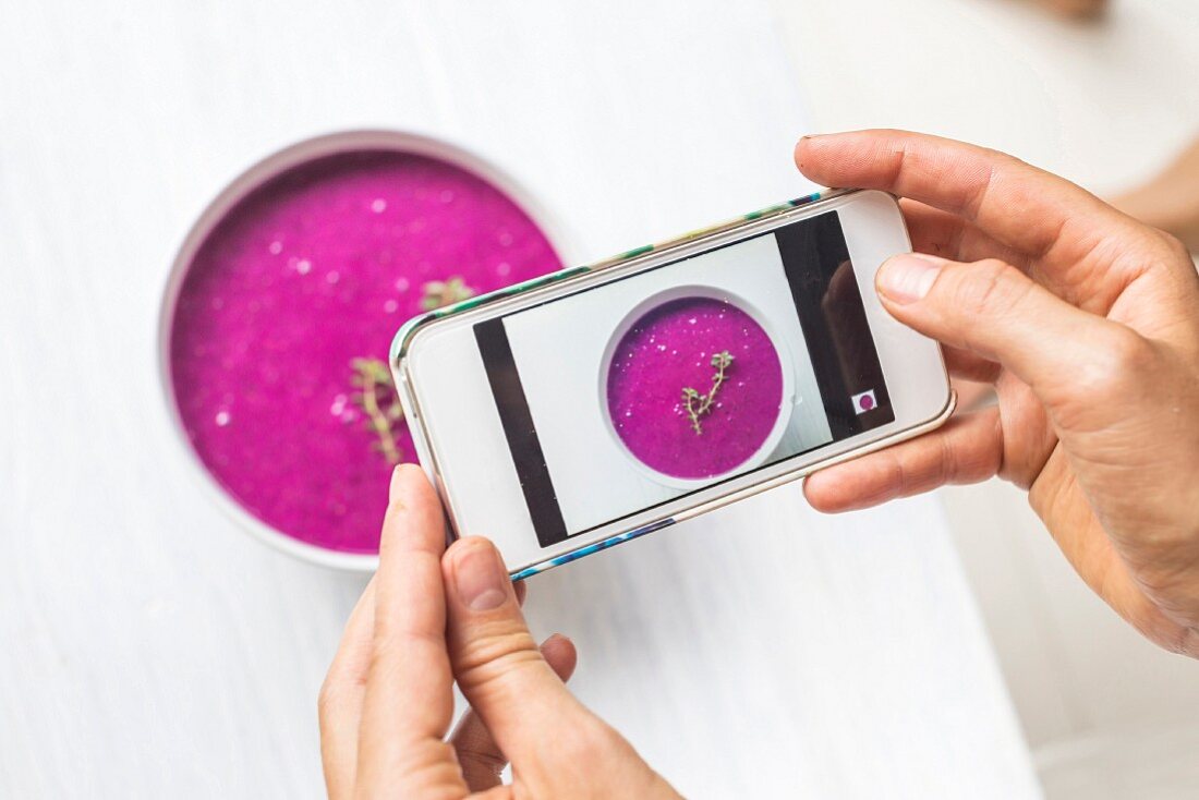 A woman using a smartphone to take a picture of a dragon fruit smoothie bowl