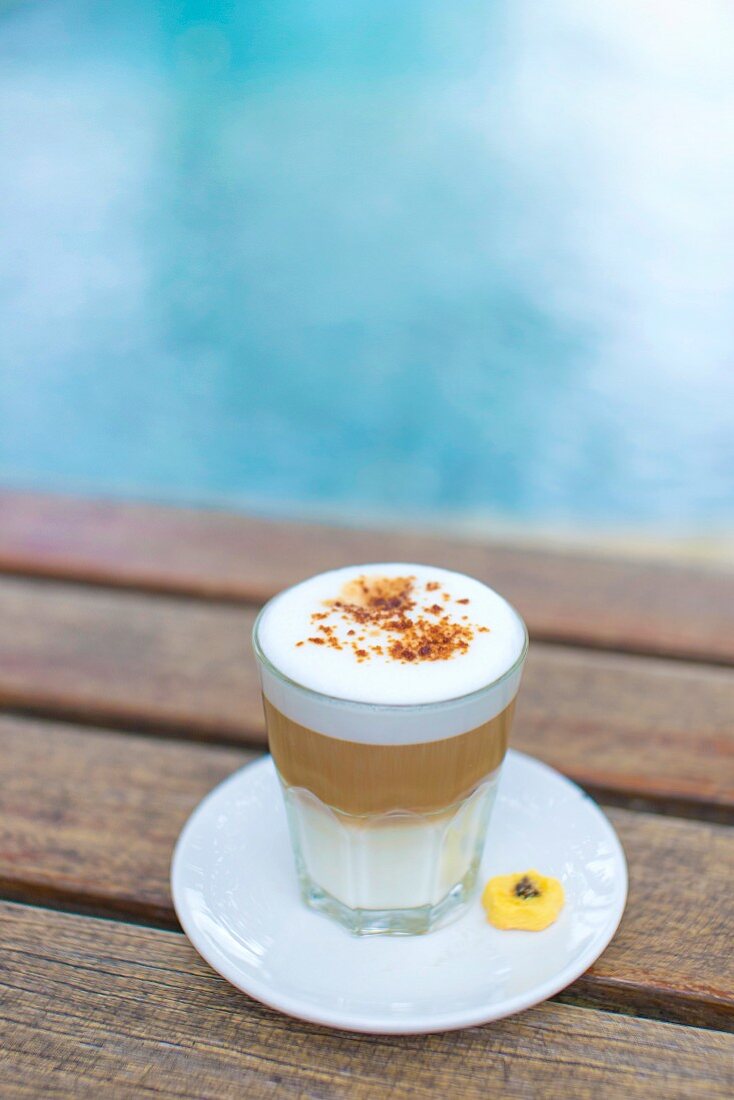 A latte backyard in a glass on a wooden table by a pool
