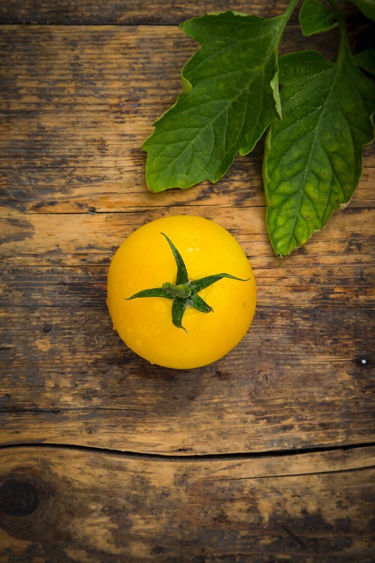 A yellow tomato on a wooden surface (seen from above)
