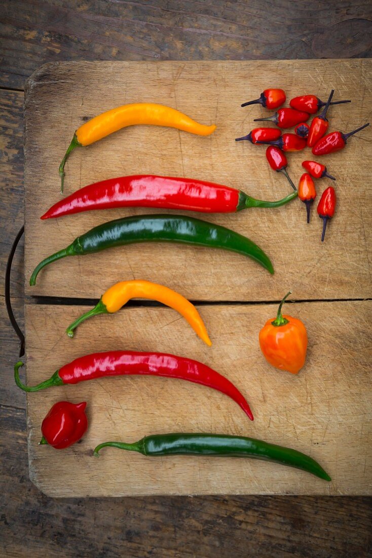 Various chilli peppers on a wooden chopping board (seen from above)