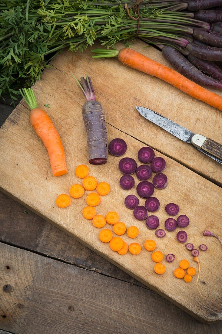 Purple and orange carrots, partially sliced, on a wooden board
