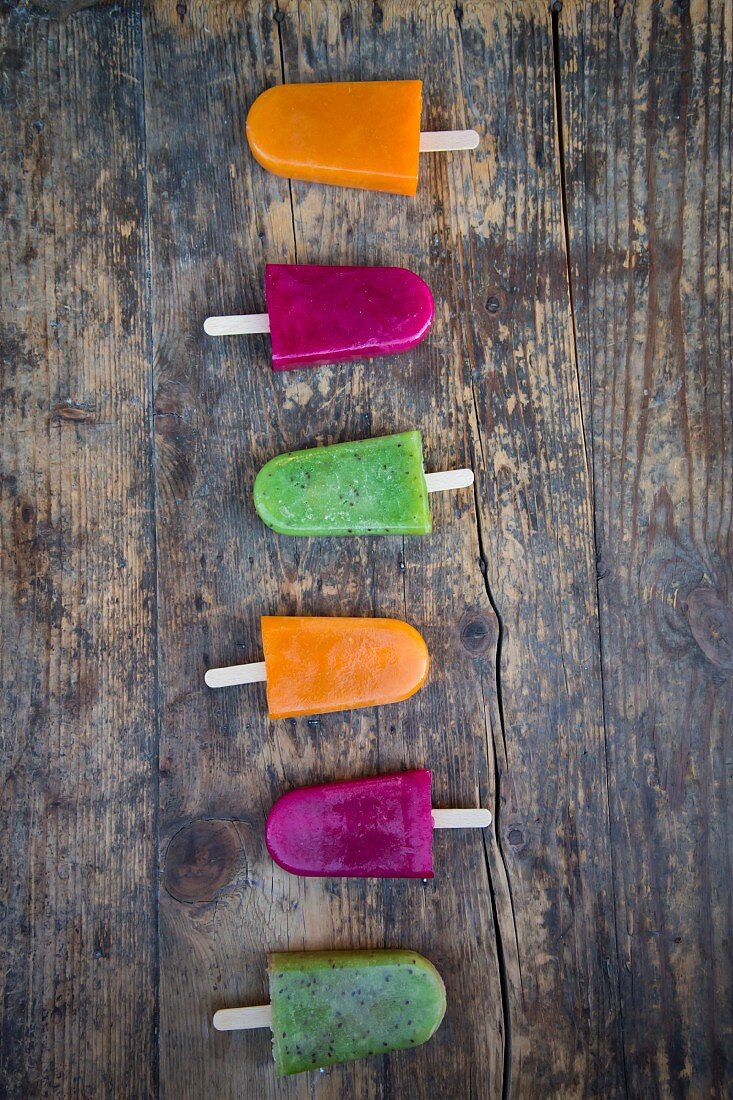 Various fruit ice lollies in a row on a wooden surface (seen from above)