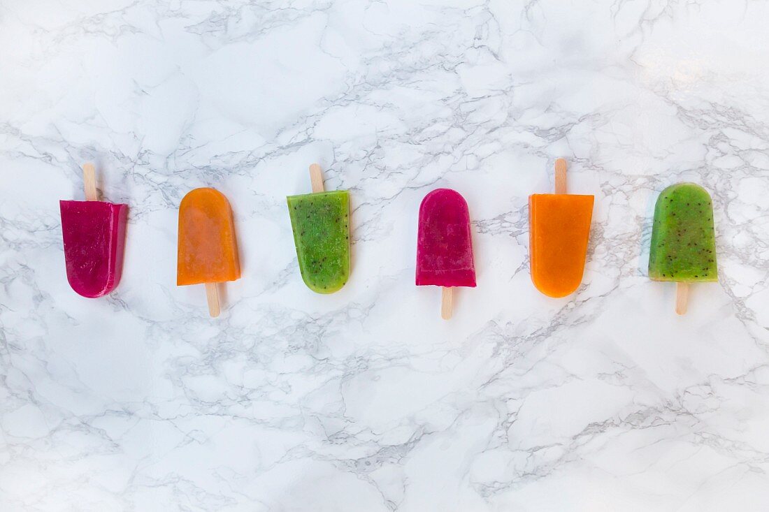 Various fruit ice lollies in a row on a marble surface