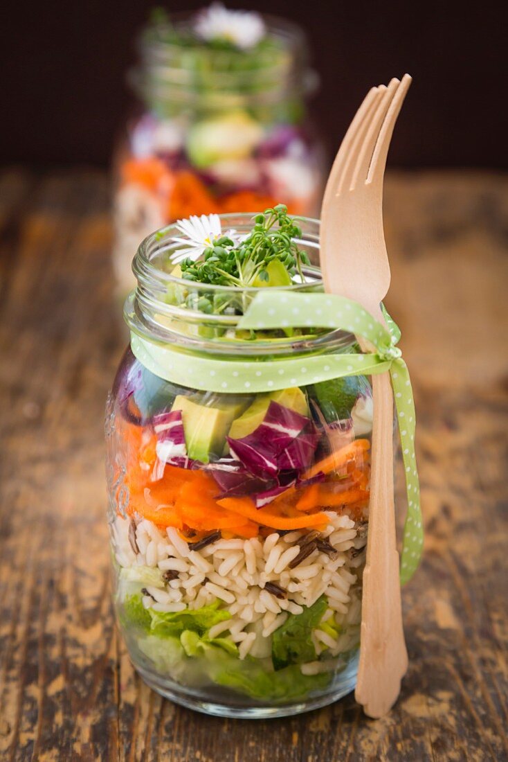 Frühlingshafter Schichtsalat mit Reis, Gemüse und Gänseblümchen in Gläsern