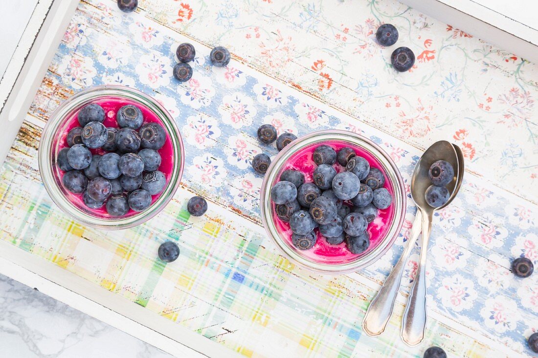 Two glasses of overnight oats with blueberries and berry juice on a wooden tray
