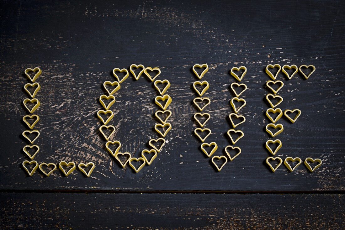 Wort Love aus herzförmigen Nudeln auf dunklem Holzuntergrund