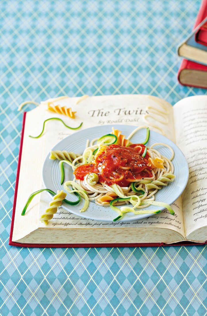 Verschiedene Nudeln mit Tomatensauce und grünen Zucchinistreifen auf aufgeschlagenem Buch
