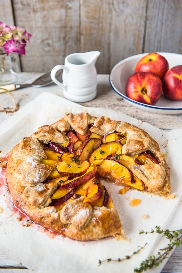 Nectarine galette, sliced, with a jug of cream and fresh nectarines