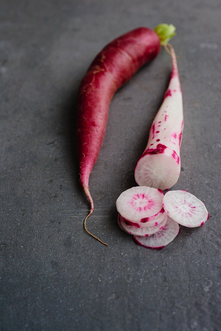 A red radish and a red and white radish on a grey surface