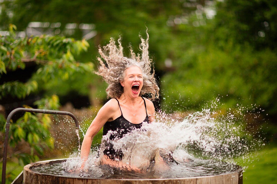 Ältere Frau im Badeanzug springt in Wasserbottich im Garten