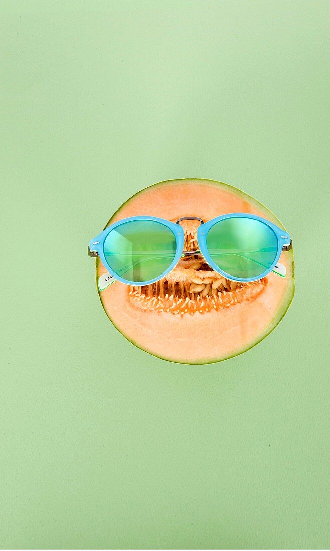 A sliced honeydew melon wearing turquoise sunglasses