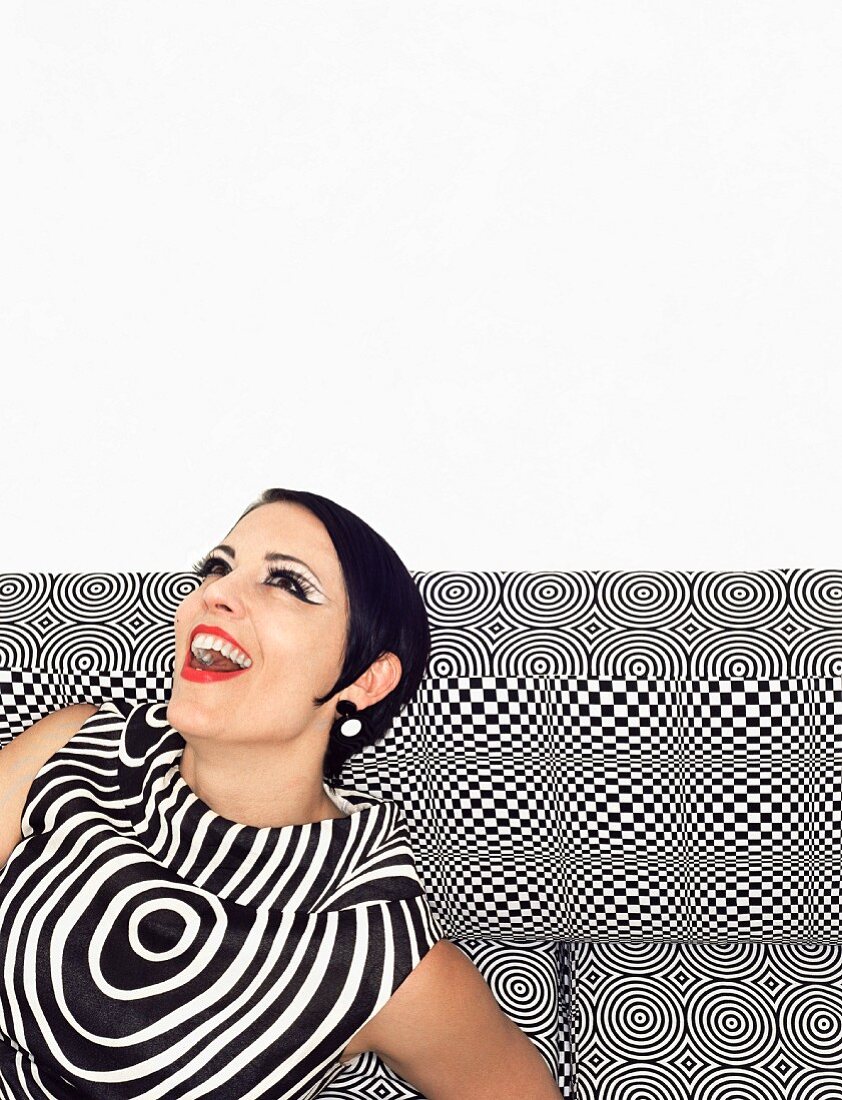 A black-haired woman wearing a black and white retro dress on a patterned sofa