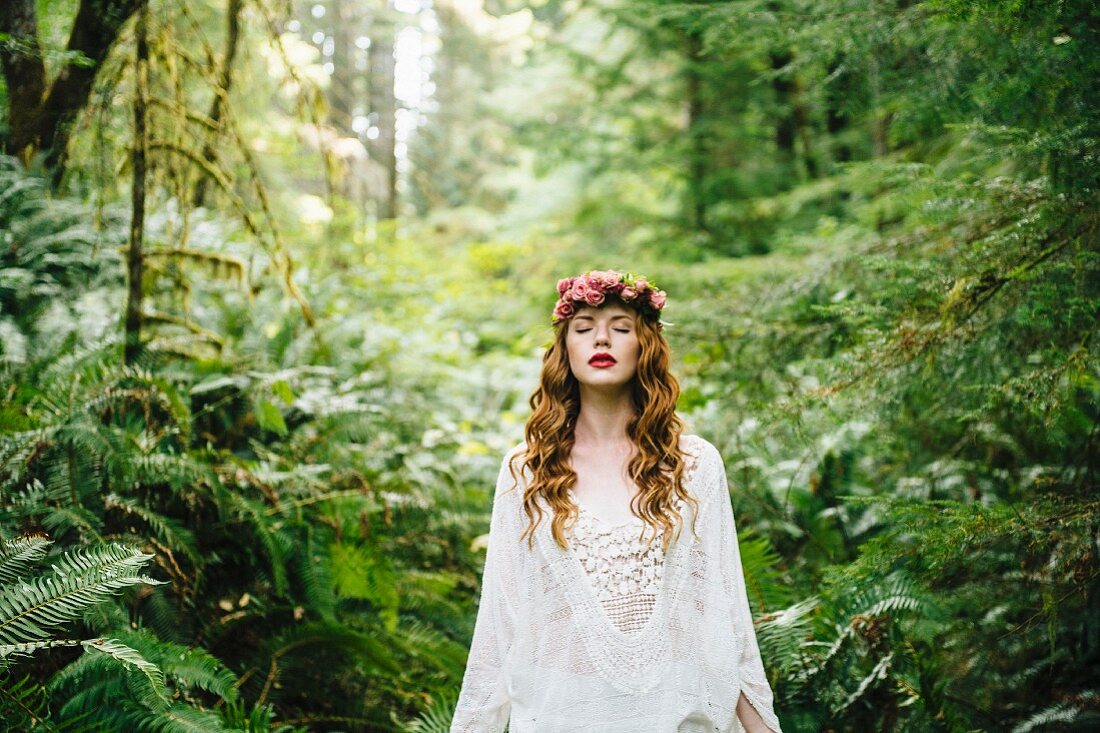 A red-haired woman wearing a crown of flowers and a white lace dress in a forest