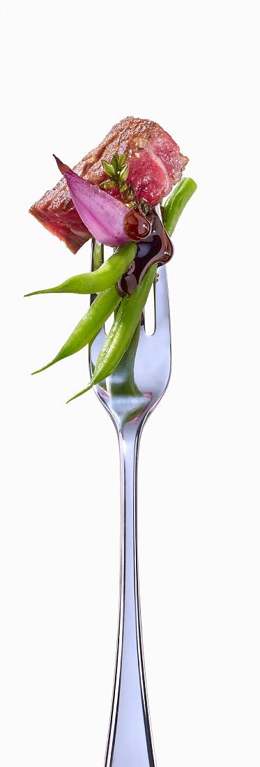 A beef steak, green beans and onions as a fork canapé