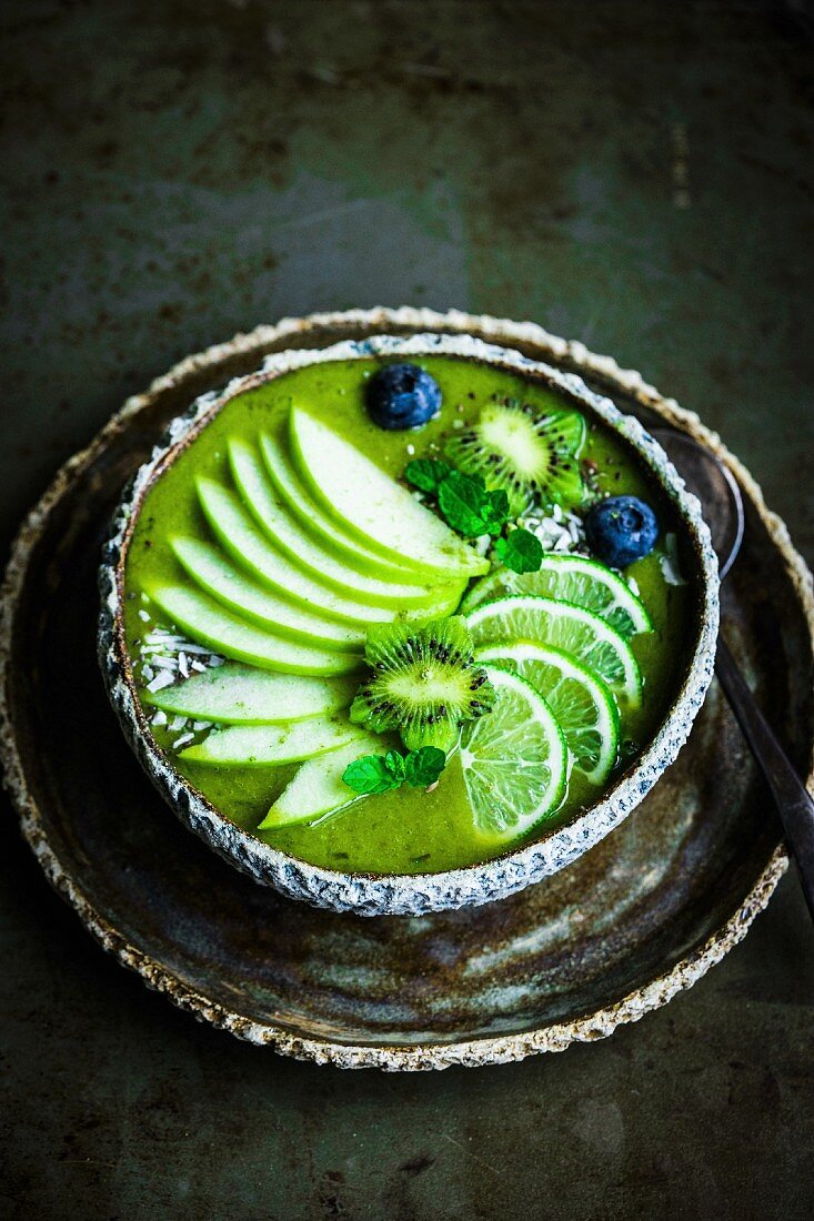 Green smoothie bowl with spinach, banana, apple, coconut water, limes, kiwi flowers and blueberries