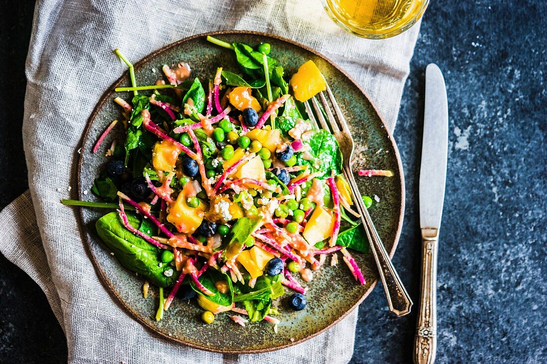 Summer rainbow salad with spinach, mango, sweet peas, blueberries, watermelon radish, blue cheese and raspberry sauce