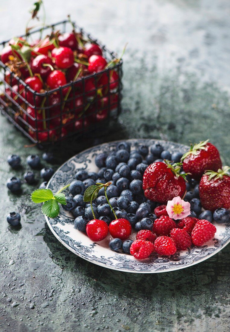 Fresh berries on a plate and sour cherries in a wire basket